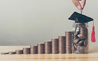 A stack of coins with a graduation cap sitting atop a coin-filled jar at the end.
