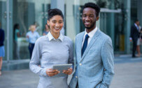 Two recent business graduates smile infront of their new place of employment.